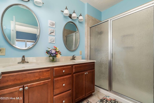 bathroom with double vanity, a textured ceiling, a stall shower, and a sink