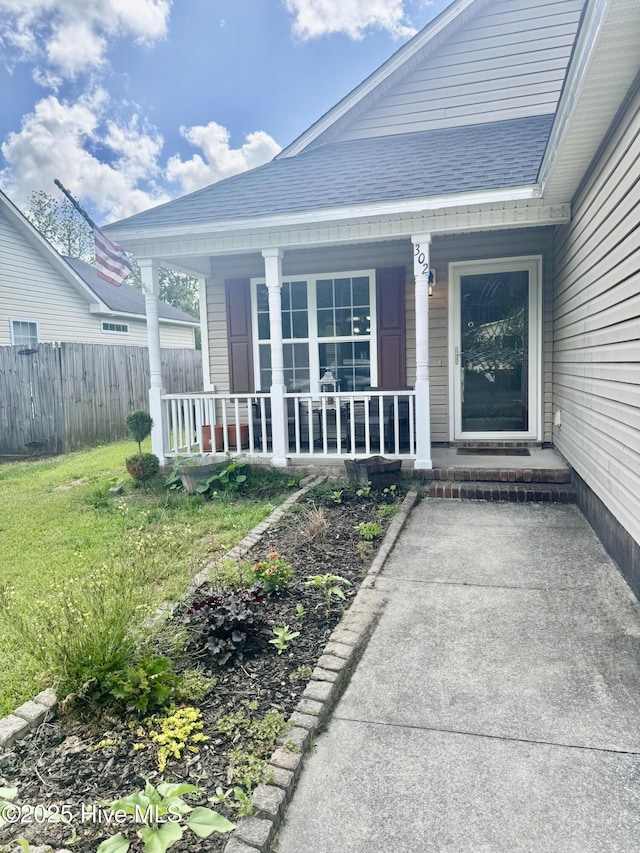 entrance to property featuring a porch, roof with shingles, and fence