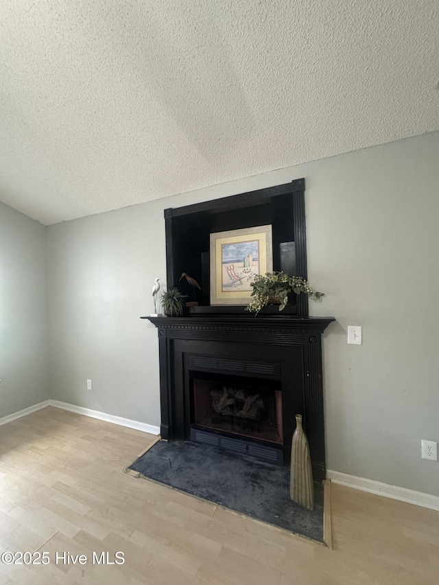 room details featuring baseboards, a fireplace with flush hearth, a textured ceiling, and wood finished floors