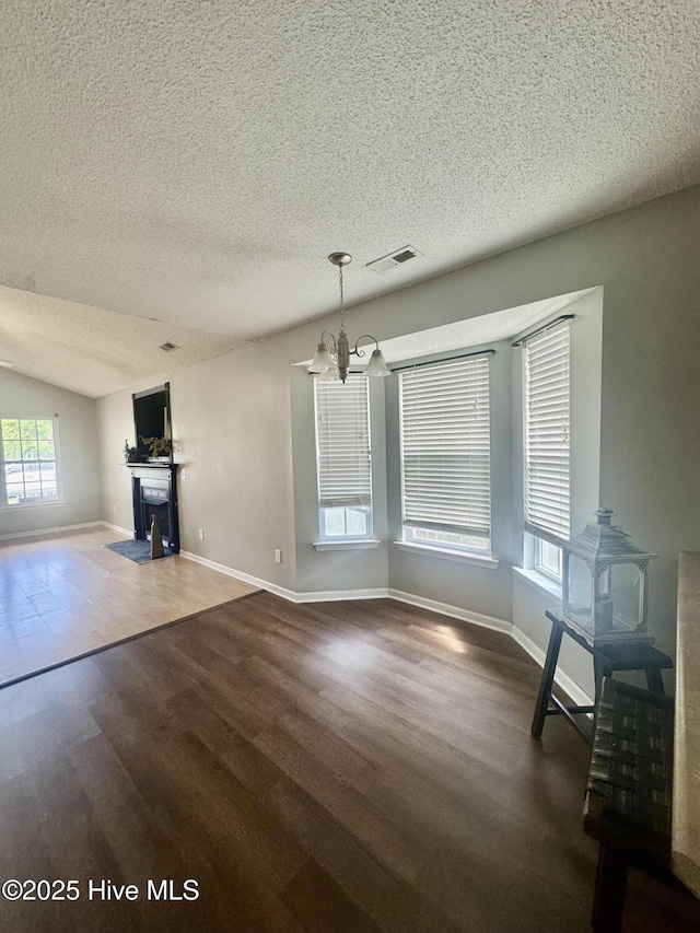 unfurnished dining area with an inviting chandelier, a textured ceiling, visible vents, and wood finished floors