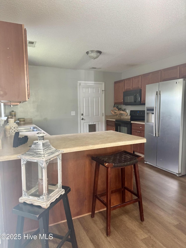 kitchen featuring black appliances, visible vents, a textured ceiling, and wood finished floors
