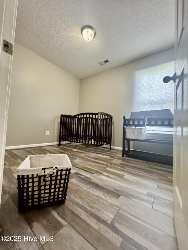 bedroom with a textured ceiling, baseboards, visible vents, and wood finished floors