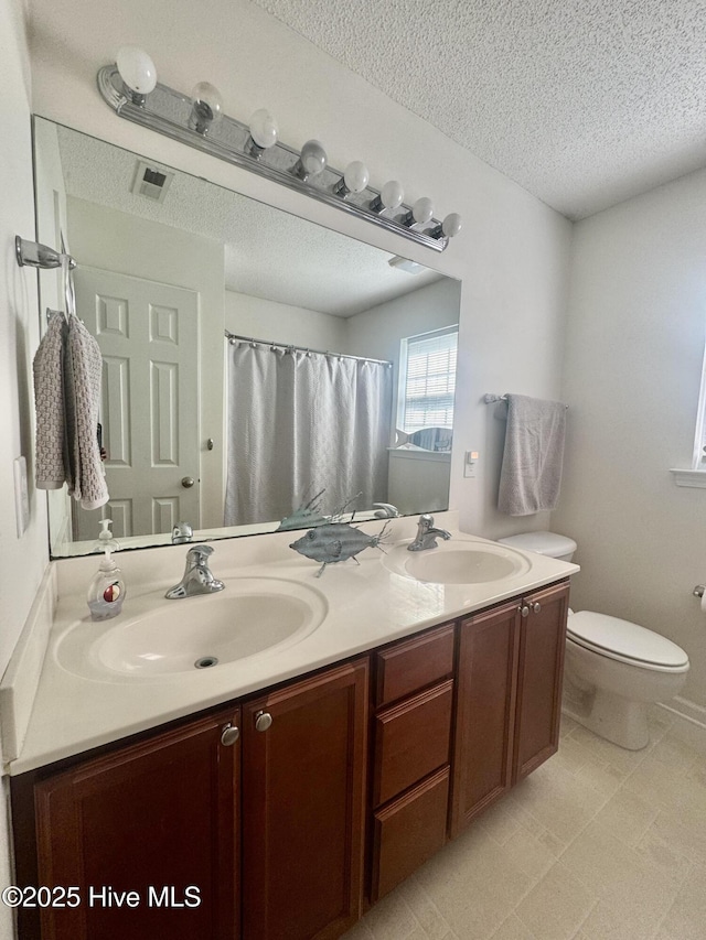 full bathroom with double vanity, a textured ceiling, toilet, and a sink