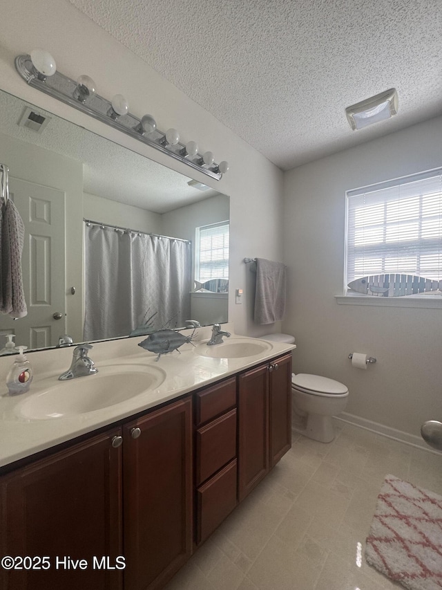 bathroom featuring double vanity, a textured ceiling, toilet, and a sink
