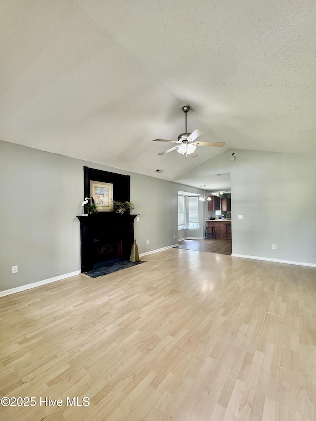 unfurnished living room featuring a ceiling fan, lofted ceiling, light wood-style flooring, and a fireplace with flush hearth