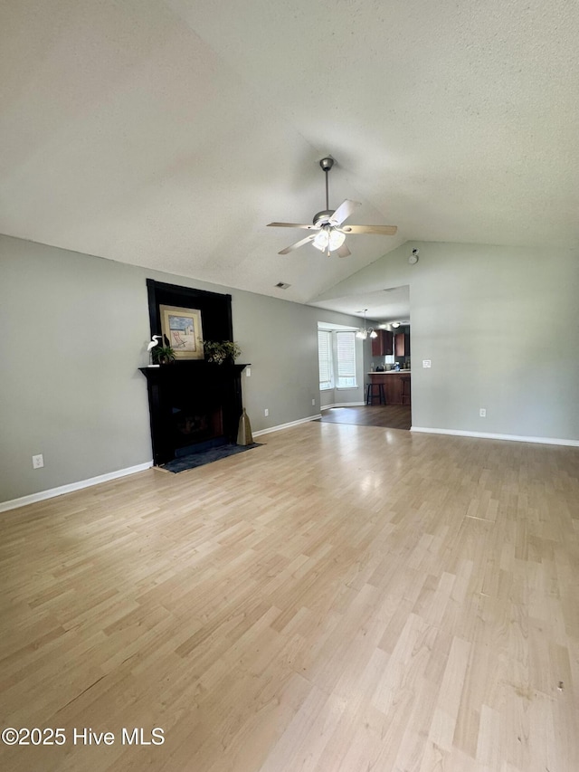 unfurnished living room featuring light wood-type flooring, vaulted ceiling, a ceiling fan, and a fireplace with flush hearth