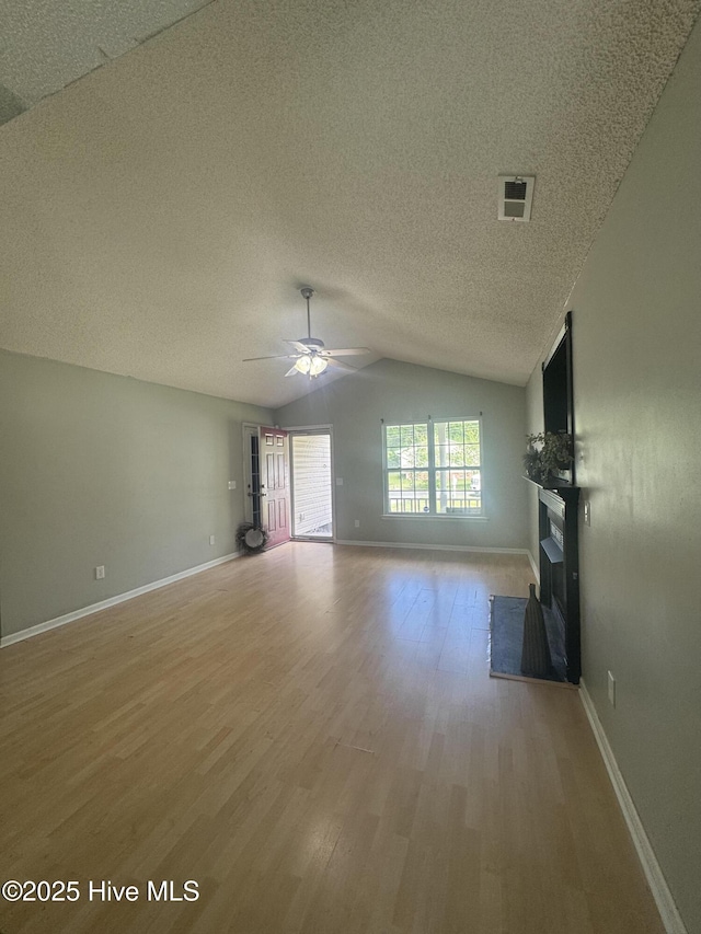 unfurnished living room with lofted ceiling, a textured ceiling, ceiling fan, a fireplace, and light wood-type flooring