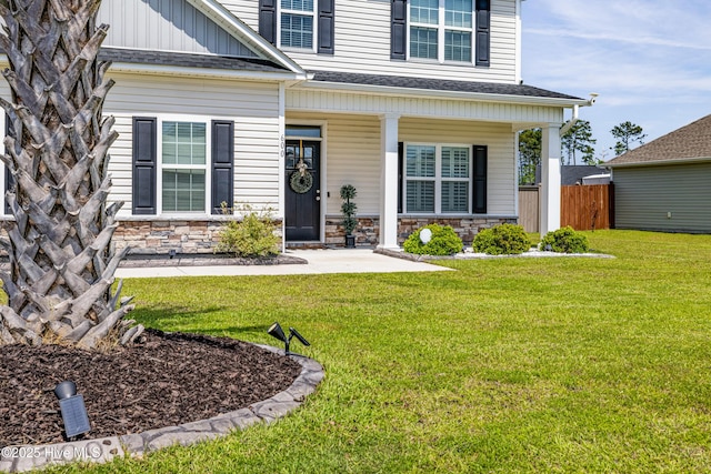 view of exterior entry featuring covered porch, fence, stone siding, and a lawn
