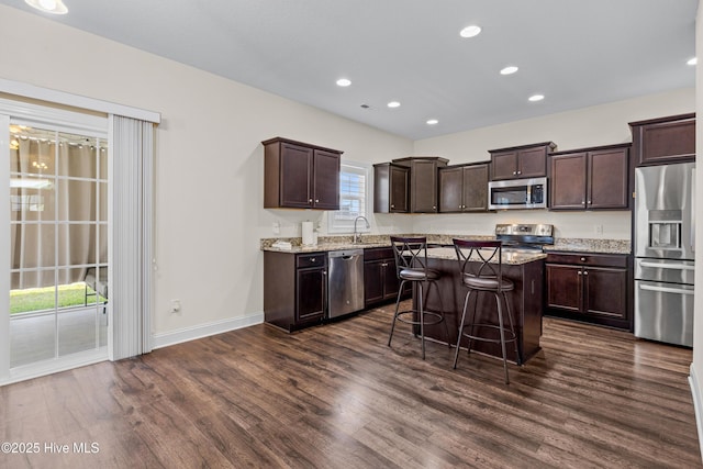 kitchen with a sink, stainless steel appliances, dark wood-style flooring, a kitchen island, and dark brown cabinets