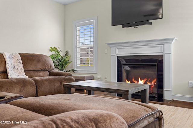 living room featuring baseboards, a glass covered fireplace, and wood finished floors
