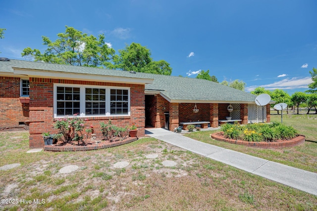 ranch-style house featuring brick siding, a front yard, and roof with shingles