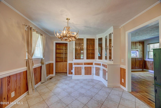 unfurnished dining area with a chandelier, wainscoting, light tile patterned floors, wood walls, and a textured ceiling
