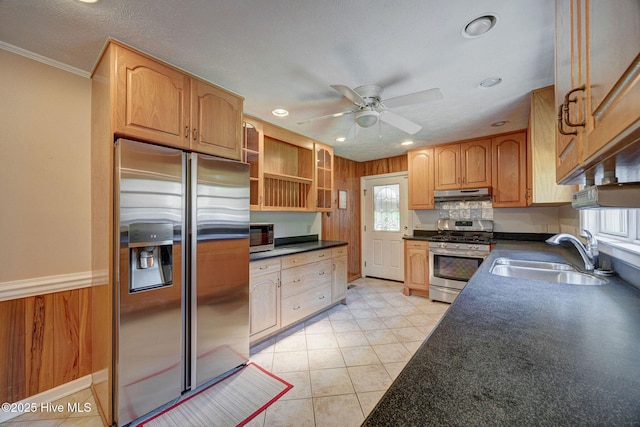 kitchen with stainless steel appliances, a sink, under cabinet range hood, dark countertops, and crown molding