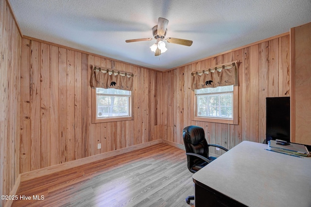 office area with plenty of natural light, wood finished floors, ceiling fan, wooden walls, and baseboards