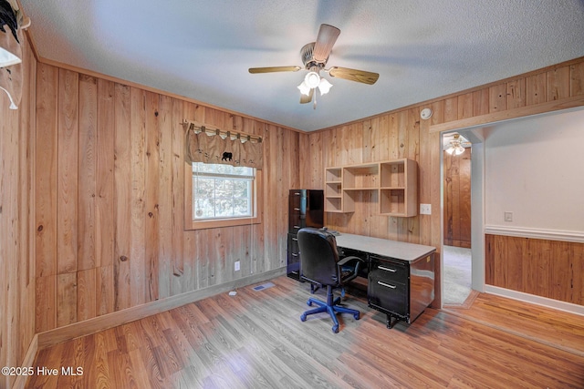office space with wooden walls, light wood finished floors, baseboards, ceiling fan, and a textured ceiling