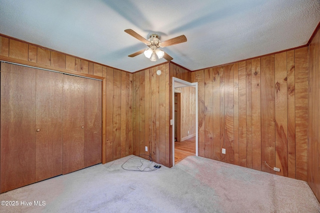 unfurnished bedroom with carpet, wood walls, a closet, and ceiling fan