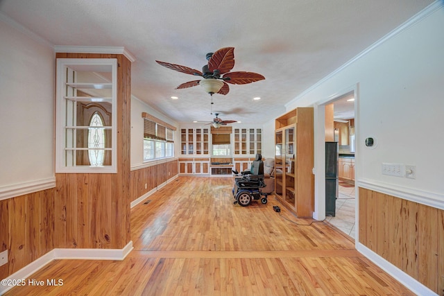 living area with wood finished floors, ceiling fan, wainscoting, ornamental molding, and wood walls