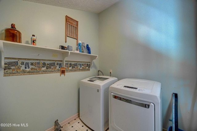 clothes washing area with washing machine and clothes dryer, a textured ceiling, and baseboards