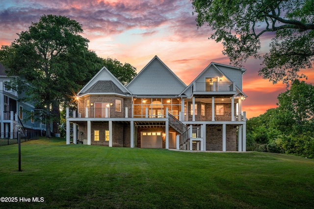 back of property at dusk featuring a garage, a lawn, brick siding, and stairway