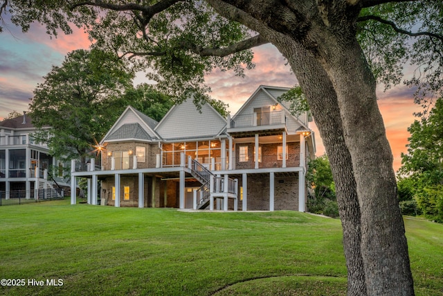 rear view of house featuring a sunroom, stairway, brick siding, and a lawn