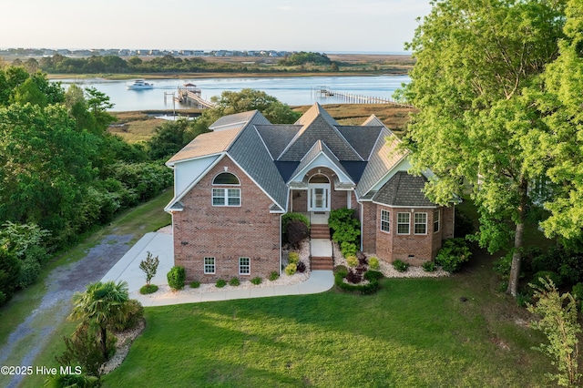 view of front of house with brick siding, a water view, and a front lawn