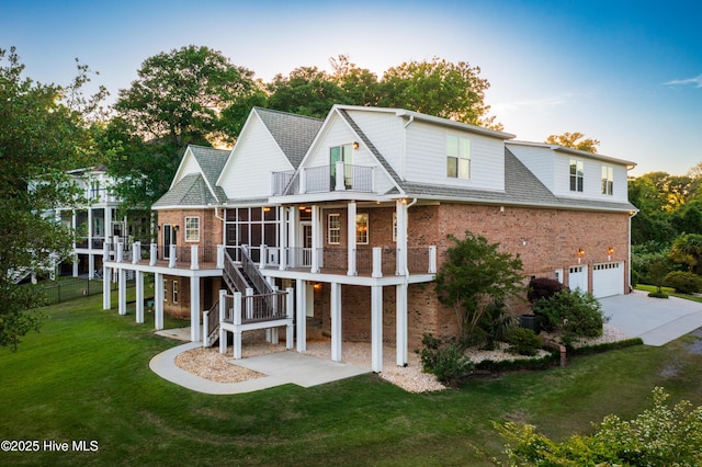 rear view of property featuring brick siding, a balcony, a garage, concrete driveway, and stairs