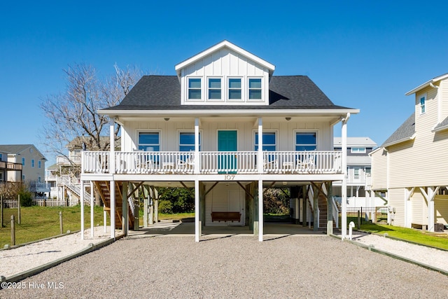 beach home featuring covered porch, stairs, a shingled roof, and a carport