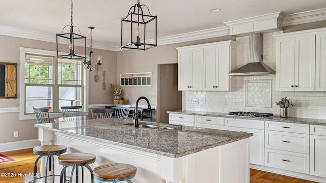 216 National Dr, Pinehurst, NC 28374 - kitchen featuring wall chimney exhaust hood, a sink, stainless steel gas cooktop, an island with sink, and white cabinetry