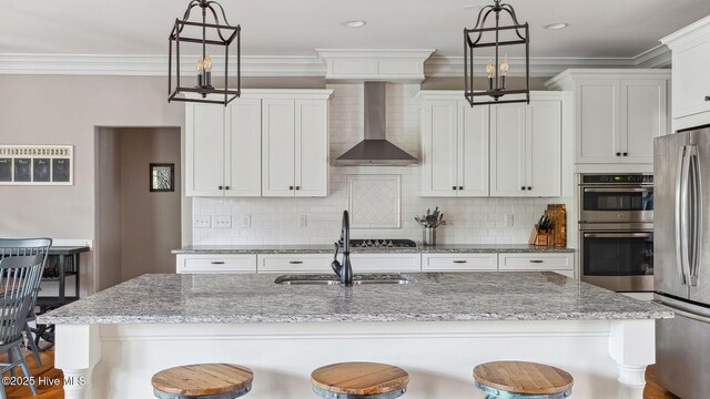 216 National Dr, Pinehurst, NC 28374 - kitchen featuring wall chimney exhaust hood, appliances with stainless steel finishes, a kitchen bar, backsplash, and white cabinets