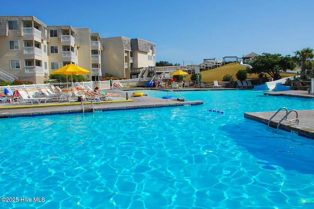 community pool featuring fence, a patio area, and a water slide