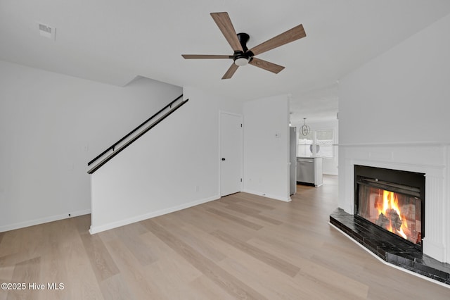 unfurnished living room featuring light wood-style floors, a lit fireplace, ceiling fan, and baseboards