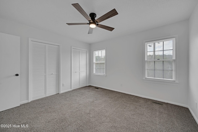 unfurnished bedroom featuring two closets, carpet floors, baseboards, and a ceiling fan