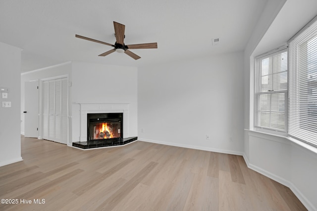 unfurnished living room featuring wood finished floors, a lit fireplace, a ceiling fan, and baseboards