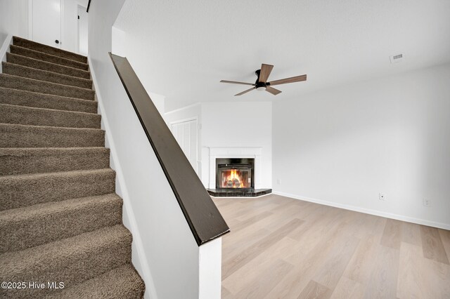 stairway with ceiling fan, wood finished floors, a glass covered fireplace, and baseboards