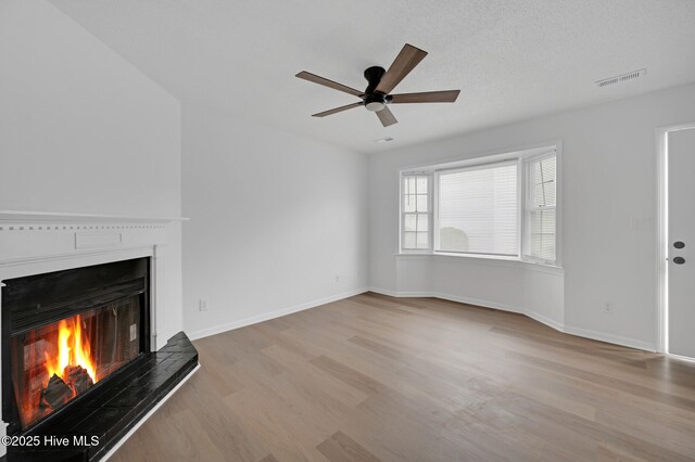 unfurnished living room featuring a lit fireplace, wood finished floors, ceiling fan, and baseboards