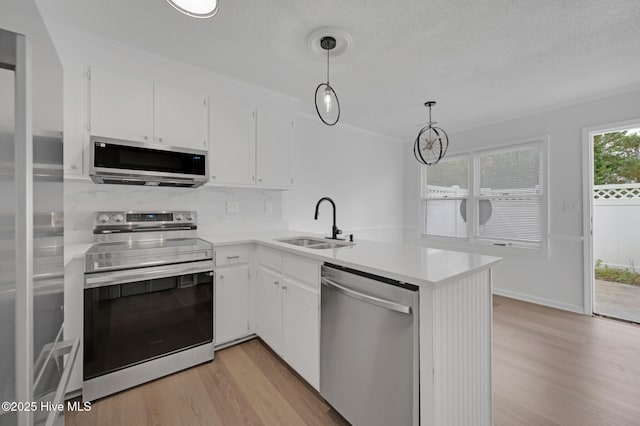 kitchen with stainless steel appliances, a sink, light wood-style flooring, light countertops, and a peninsula