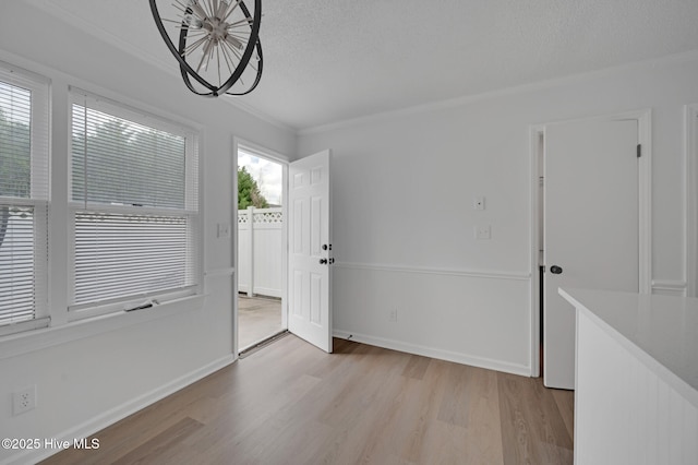unfurnished dining area featuring light wood-type flooring, baseboards, a textured ceiling, and crown molding