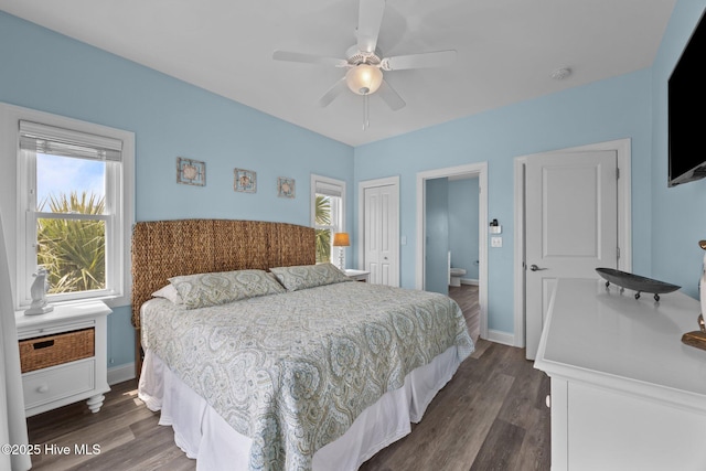 bedroom with dark wood-style floors, a closet, baseboards, ensuite bathroom, and a ceiling fan