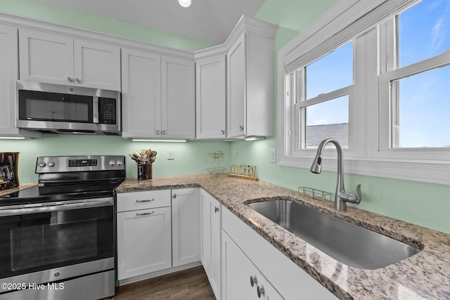 kitchen featuring stainless steel appliances, a sink, white cabinets, light stone counters, and dark wood-style flooring