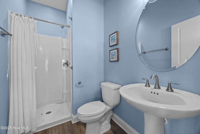 bathroom with baseboards, wood finished floors, toilet, a stall shower, and a sink