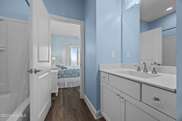 ensuite bathroom featuring wood finished floors, vanity, baseboards, and bathing tub / shower combination