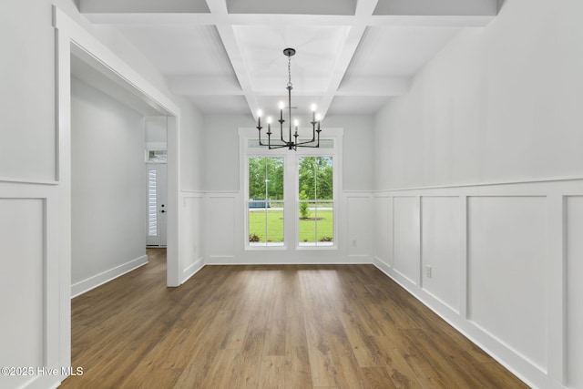 unfurnished dining area with coffered ceiling, a chandelier, wood finished floors, beamed ceiling, and a decorative wall