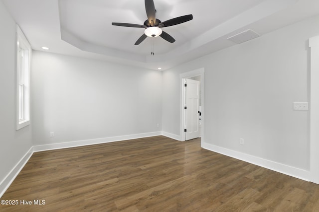 empty room featuring a raised ceiling, a ceiling fan, baseboards, dark wood-style floors, and recessed lighting