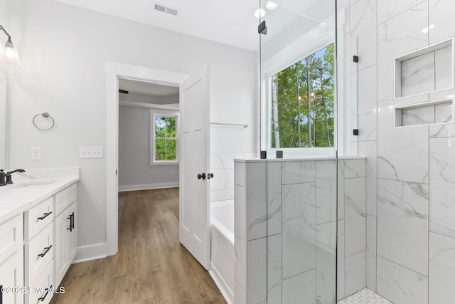 bathroom featuring wood finished floors, vanity, a marble finish shower, a garden tub, and baseboards