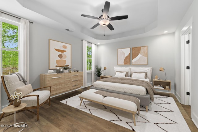bedroom featuring wood finished floors, a raised ceiling, recessed lighting, a ceiling fan, and baseboards