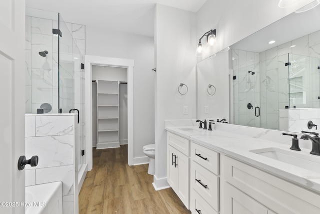 bathroom featuring a stall shower, a walk in closet, wood finished floors, double vanity, and baseboards