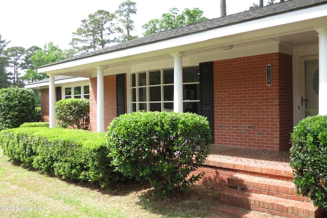 view of exterior entry featuring brick siding and a porch