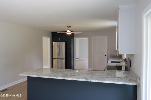 kitchen with freestanding refrigerator, ceiling fan, light wood-style flooring, light stone countertops, and a peninsula