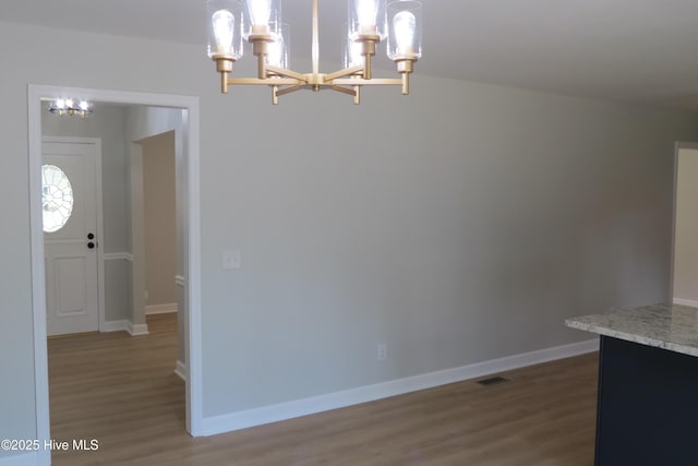 unfurnished dining area featuring a chandelier, wood finished floors, and baseboards