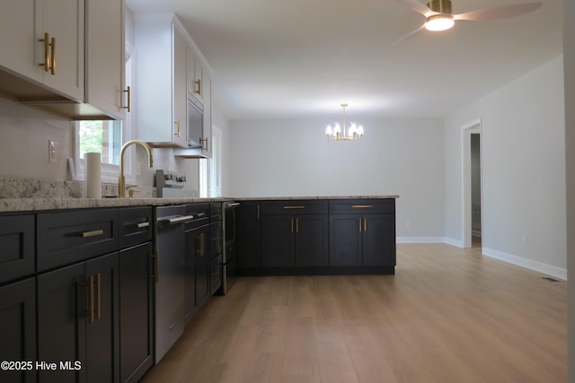 kitchen with light wood-style flooring, a peninsula, light stone counters, a chandelier, and a sink